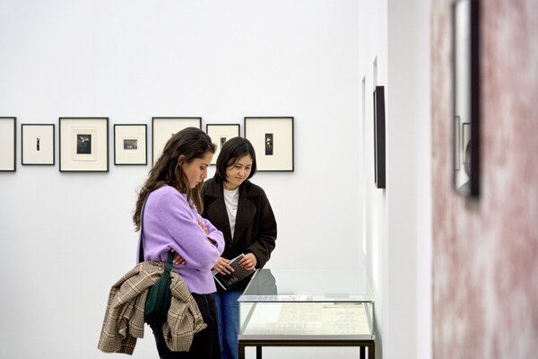 Zwei Personen betrachten in einer Galerie gerahmte Bilder und eine Vitrine