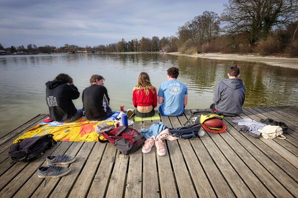 Jugendliche sitzen auf einem Streg am Wasser