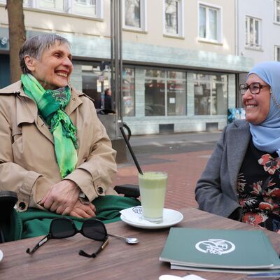 Zwei &auml;ltere Menschen unterhalten sich an einem Tisch vor einem Cafe
