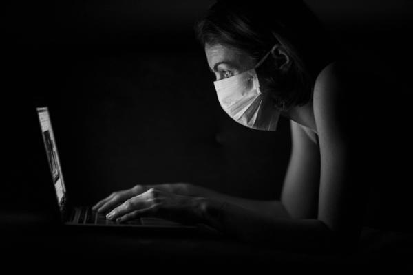 Frau mit Mundschutz an einem Laptop