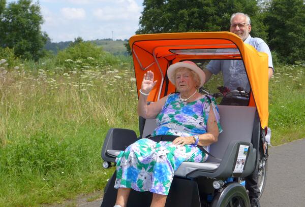 Seniorin in einer E-Rikscha mit Fahrer unterwegs in der Natur