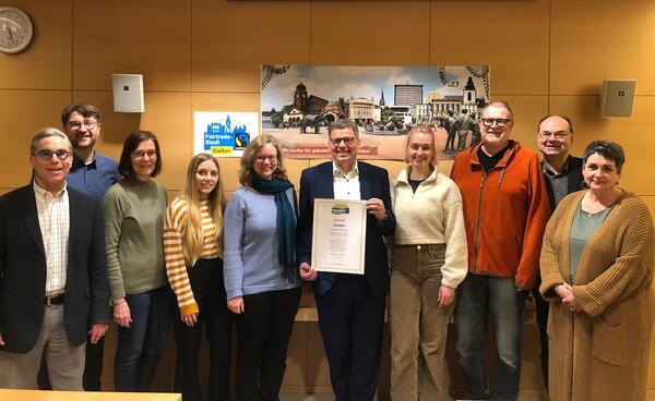 Oberbürgermeister Frank-Tilo Becher freut sich mit der Steuerungsgruppe Fairtrade Town Gießen über die Titelerneuerung "Fairtrade-Stadt" und hält die Urkunde in der Hand