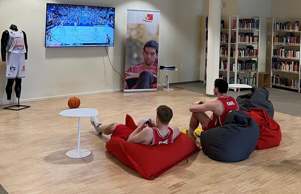 Luca Finn Kahl und Luis Elias Figge vom Team der GIESSEN 46ers spielen Basketball auf einer Konsole in der Stadtbibliothek. Das Bild ist im Februar 2024 beim Dreh f�r ein Werbevideo f�r ein E-Basketballturnier in der Stadtbibliothek entstanden.