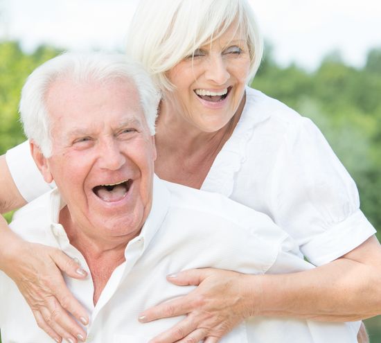 Ein &auml;lteres Paar - Ein Senior tr&auml;gt eine Seniorin l&auml;chelnd auf den Schultern