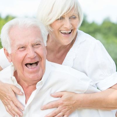 Ein &auml;lteres Paar - Ein Senior tr&auml;gt eine Seniorin l&auml;chelnd auf den Schultern