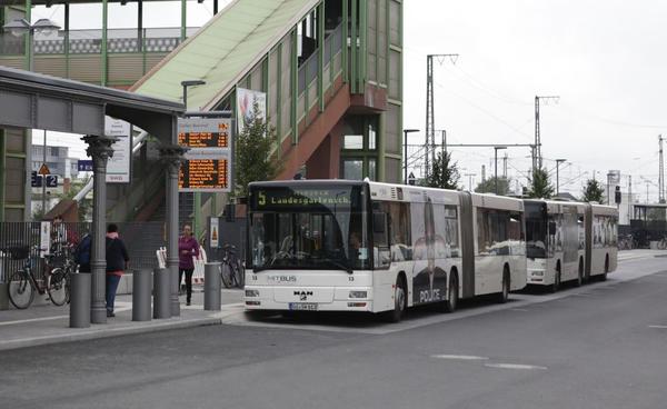 Busse der MitBus warten am Bahnhof - im Vordergrund die digitale Anzeigentafel mit den Abfahrtszeiten