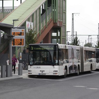 Busse der MitBus warten am Bahnhof - im Vordergrund die digitale Anzeigentafel mit den Abfahrtszeiten