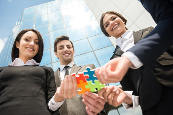 Closeup of business people wanting to put four pieces of puzzle together. Team work.